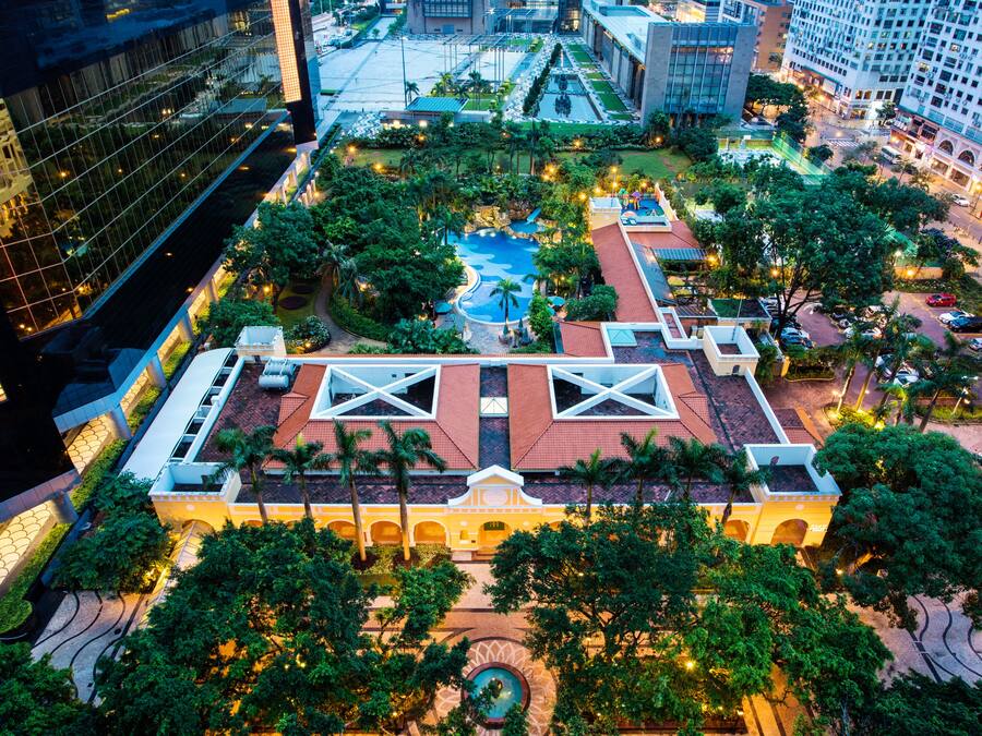 An aerial view of a hotel with a central courtyard, a swimming pool, and surrounding greenery.
