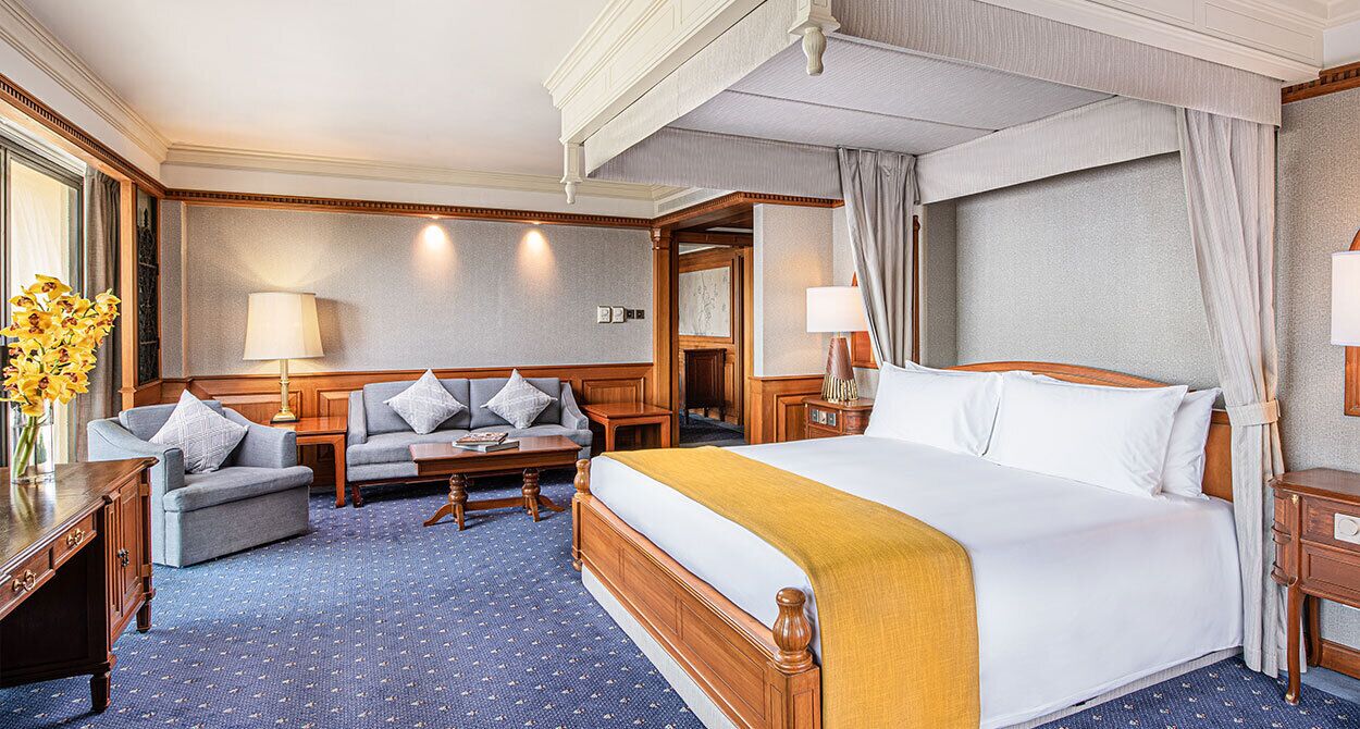 A hotel room with a large bed, a sofa, a small table, and a desk.