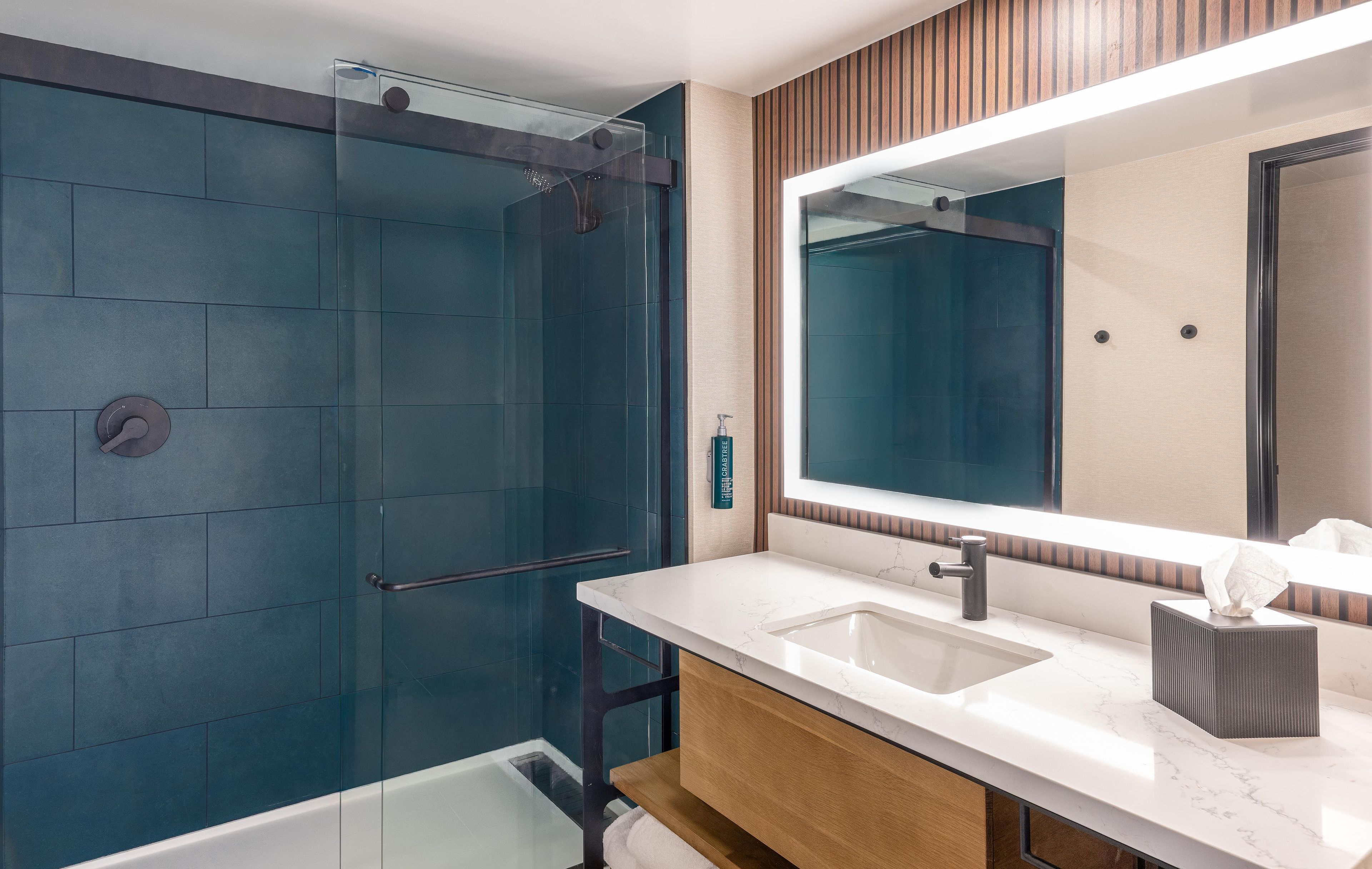 A modern bathroom with a glass shower enclosure, a large mirror, and a marble sink.