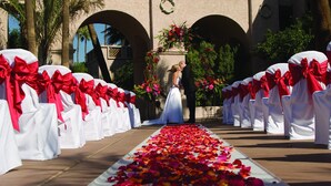 A wedding aisle with white chairs and red bows, a couple kissing, and a floral arch. - Hilton Phoenix Resort at the Peak (Phoenix)