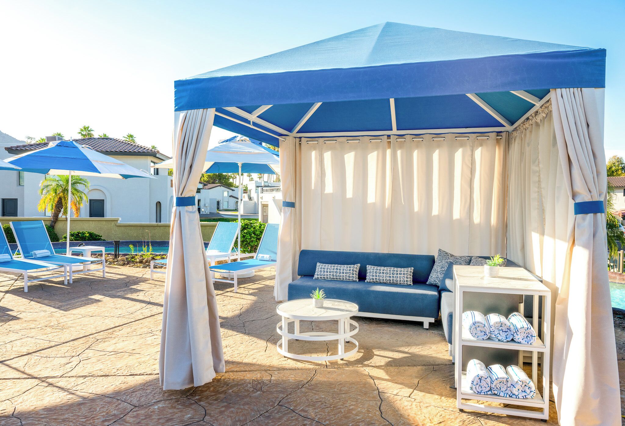 A covered outdoor seating area with a pool, lounge chairs, and a sofa.