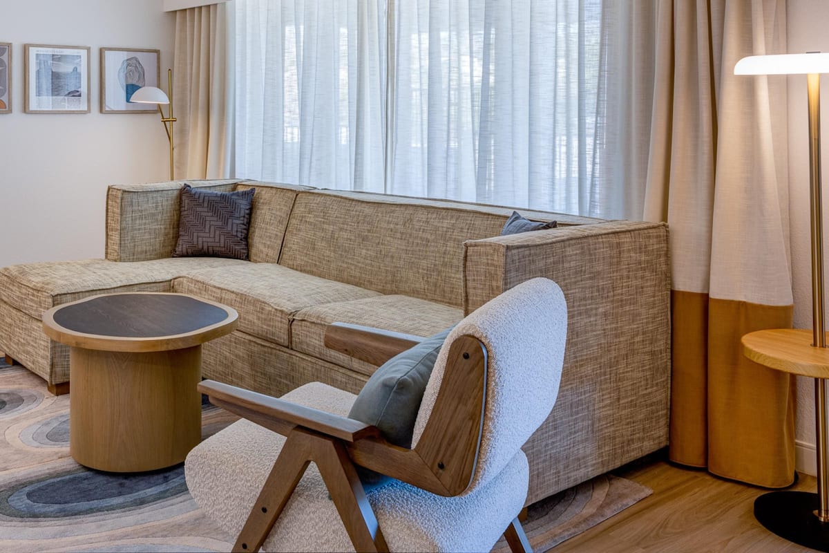A modern living room with a sectional sofa, a round coffee table, a floor lamp, and a large window with curtains.