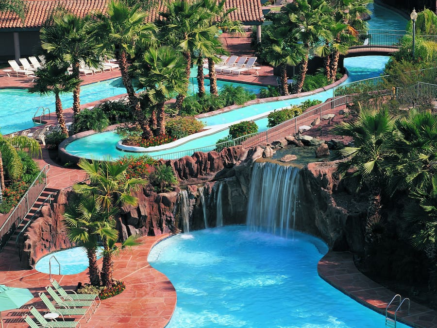 A resort with multiple swimming pools, a waterfall, and palm trees.