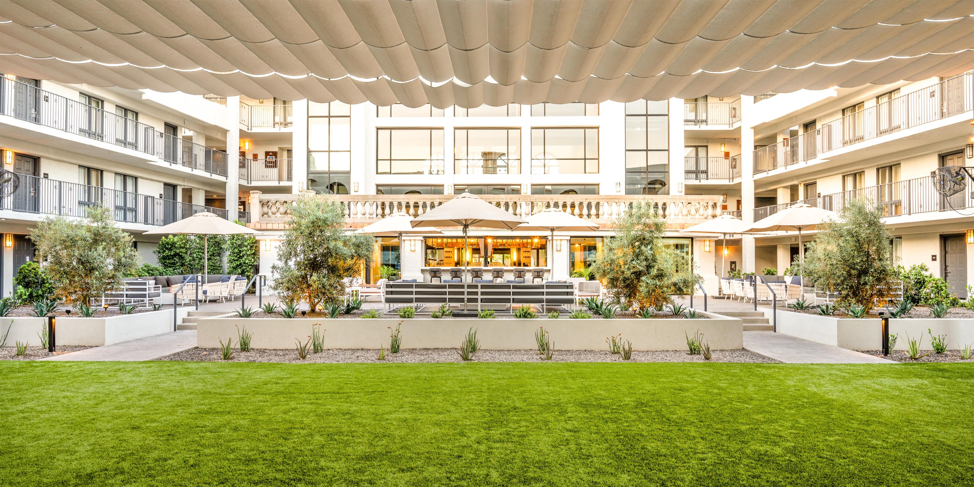 A hotel courtyard with outdoor seating, a bar, and a pool area.