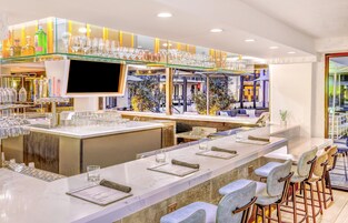 A modern bar area with a long counter, multiple glasses, and a television screen.