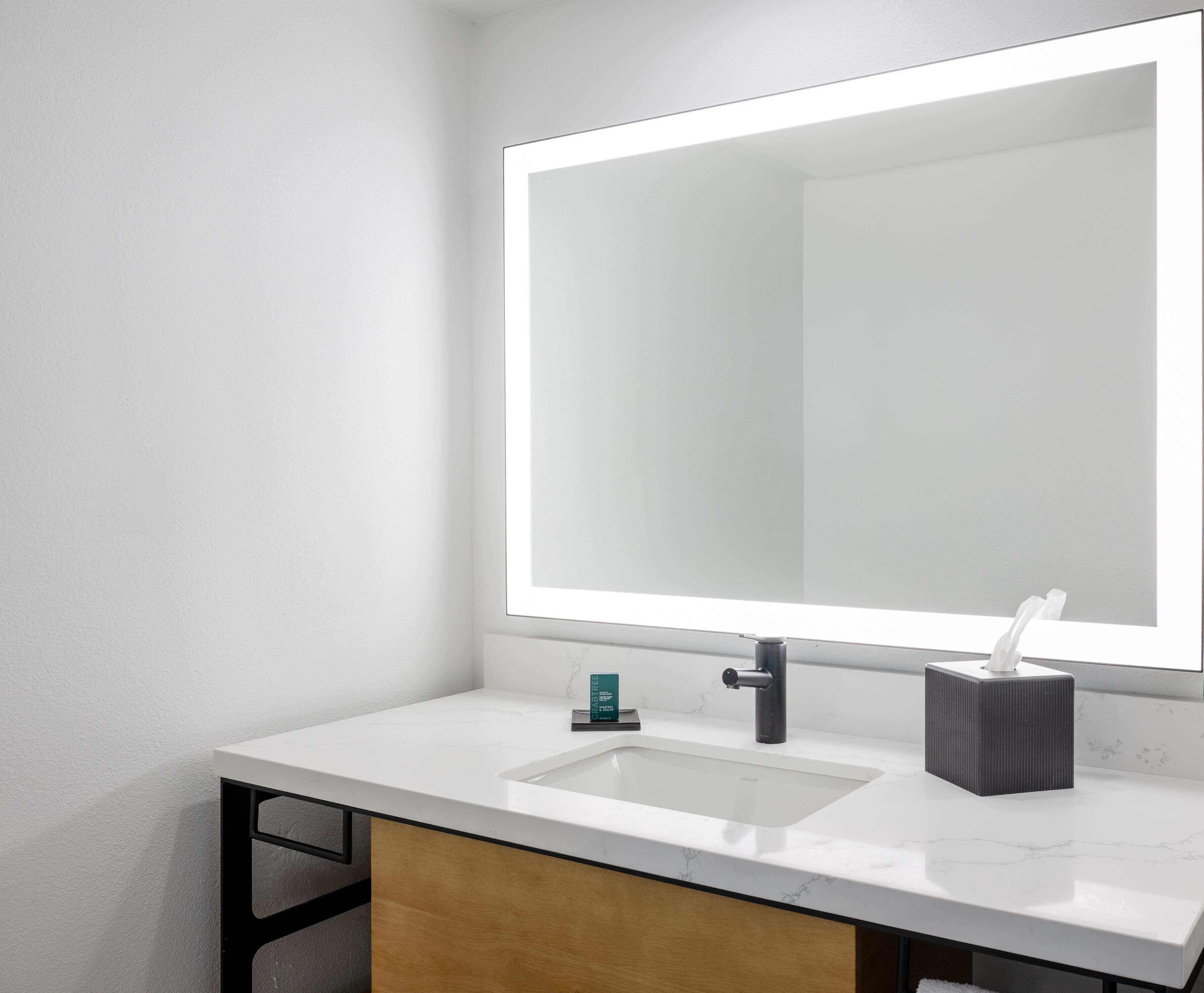 A modern bathroom with a white marble sink, a large mirror, and a towel dispenser.