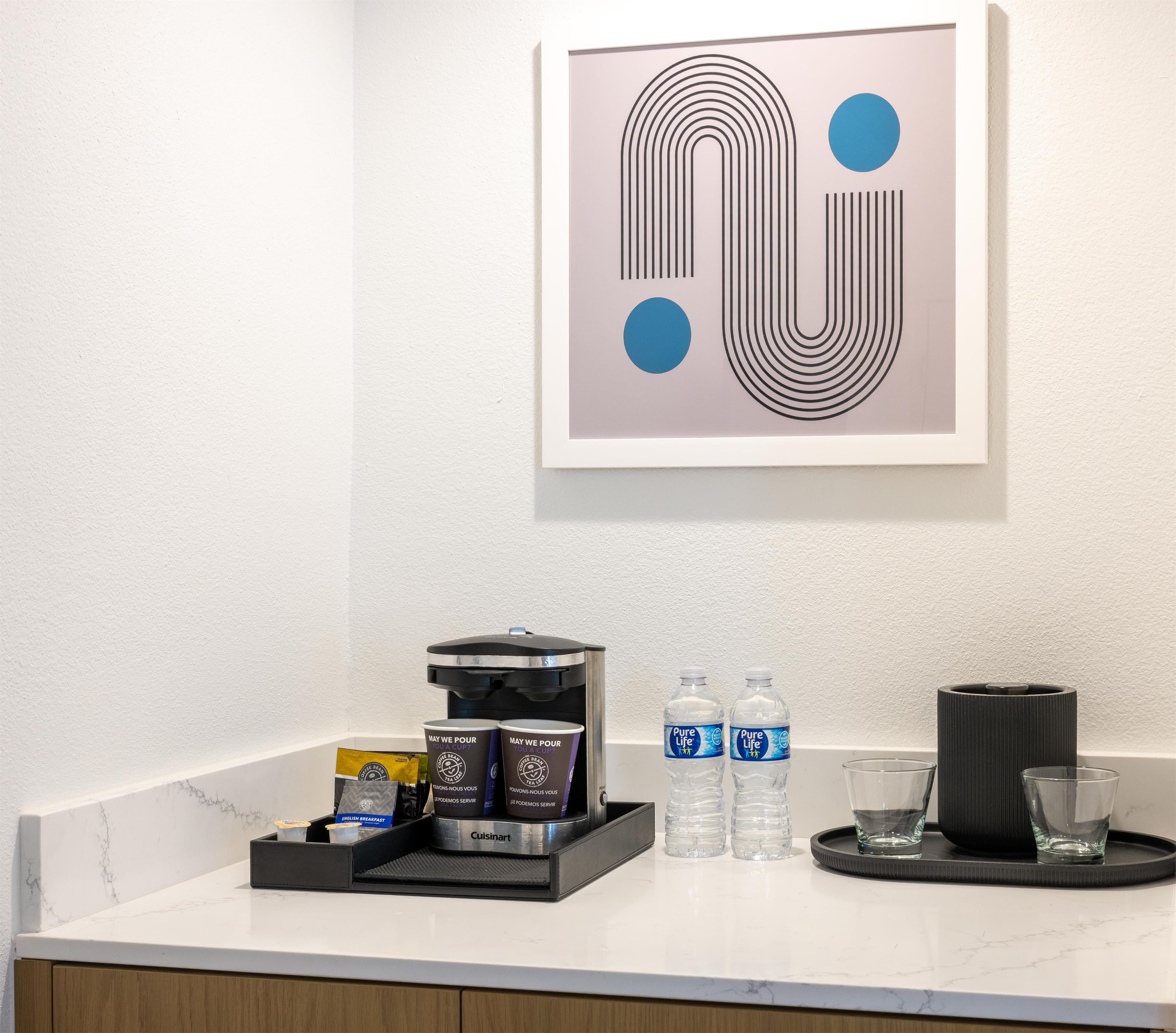 Mostrador de hotel con una máquina de café, botellas de agua y una bandeja con vasos.
