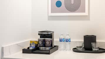 A hotel room counter with a coffee machine, water bottles, and a tray with glasses.