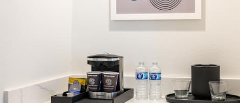 Mostrador de hotel con una máquina de café, botellas de agua y una bandeja con vasos.
