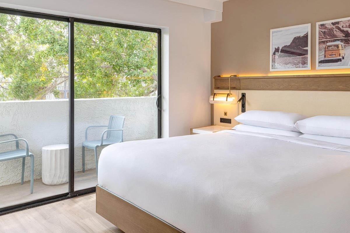 A hotel room with a large bed, a balcony with chairs, and two framed pictures on the wall.