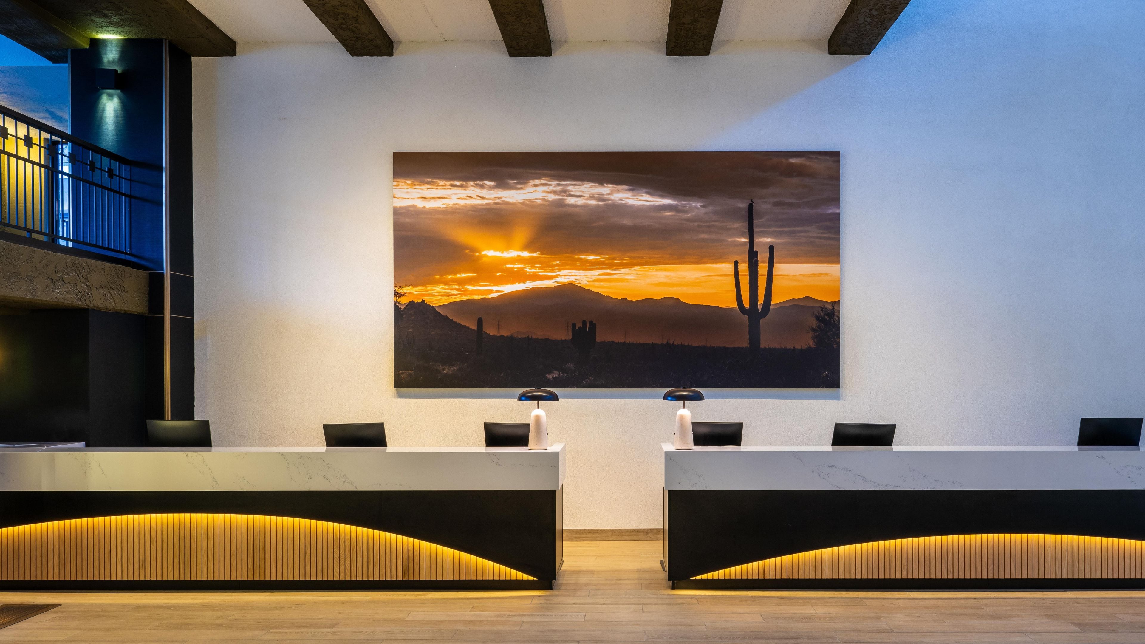 A reception area with a large desert sunset painting, two reception desks, and a modern design with wooden accents.