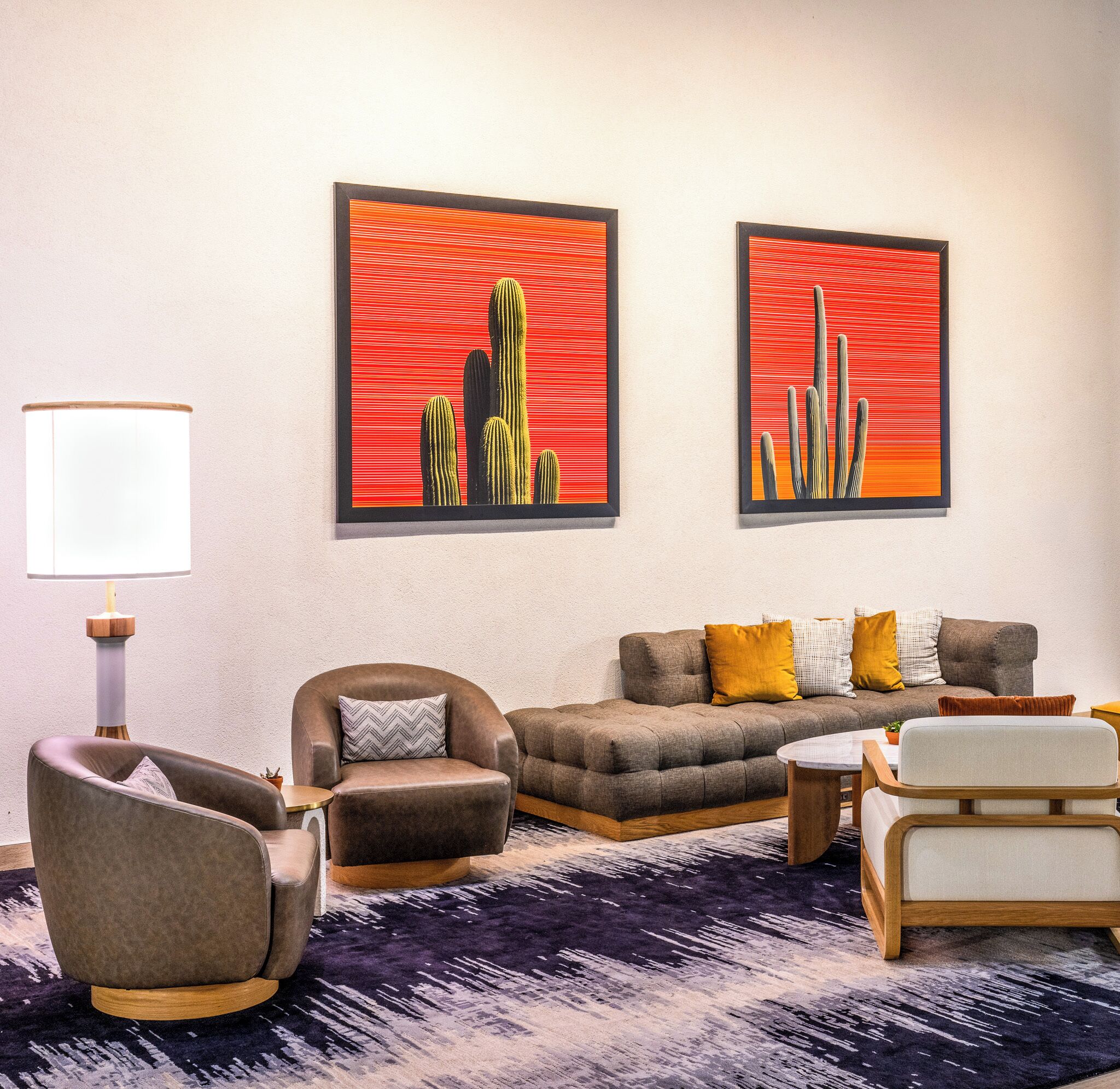 Un salon comprenant un canapé, des fauteuils, une lampe et deux œuvres d’art encadrées.