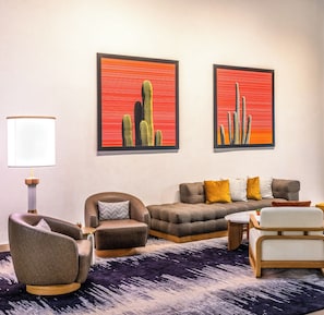 Un salon comprenant un canapé, des fauteuils, une lampe et deux œuvres d’art encadrées.