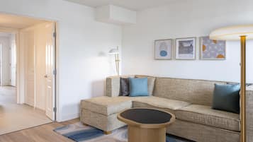 A living room with a sofa, a coffee table, and a lamp. There are framed pictures on the wall.