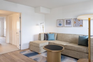 A living room with a sofa, a coffee table, and a lamp. There are framed pictures on the wall.