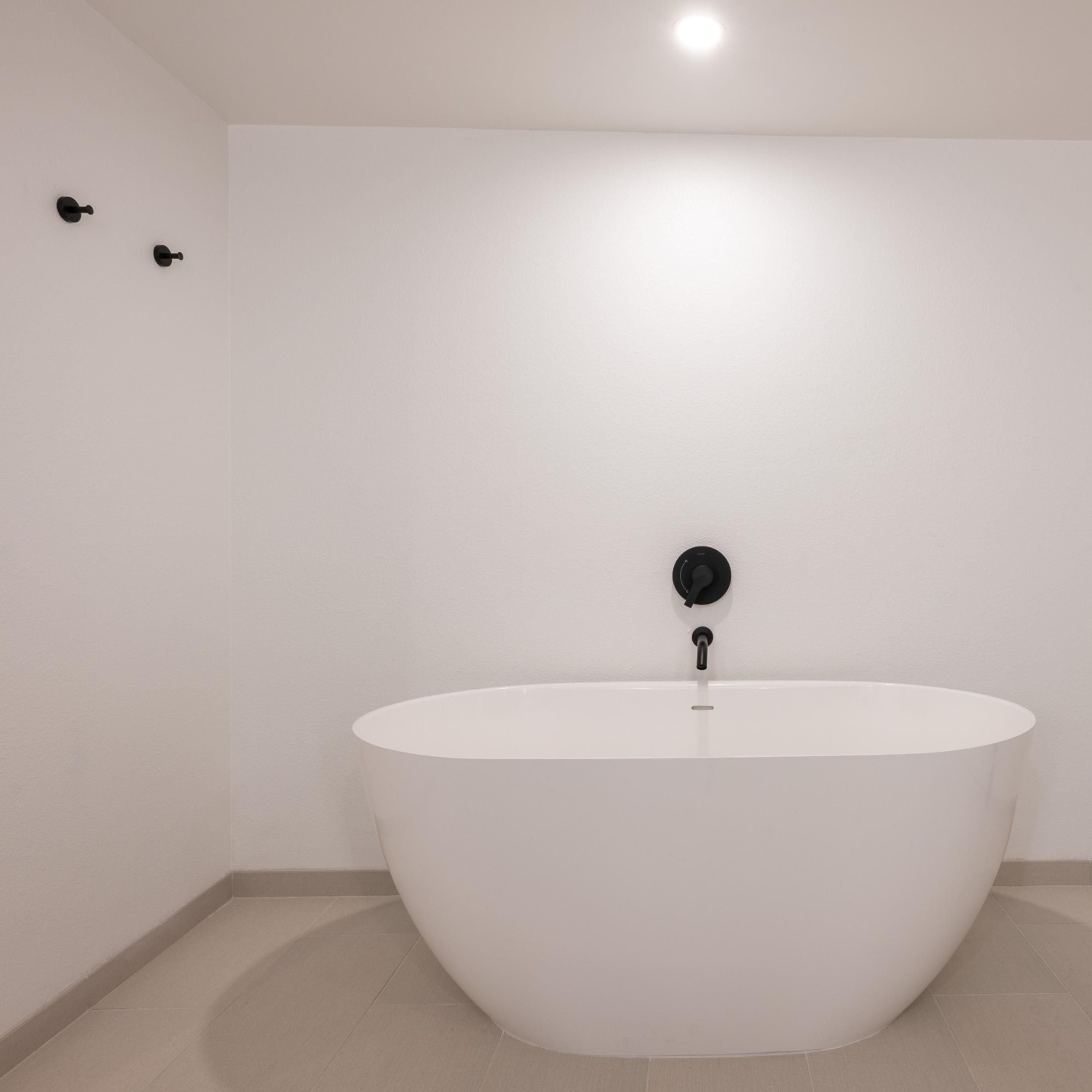 Un baño moderno con una bañera independiente, un grifo de pared y una lámpara en el techo.