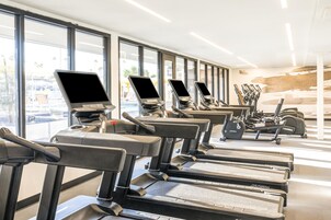 A gym with treadmills and exercise equipment, large windows, and a view of the outside.