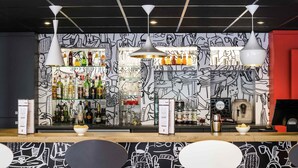 Um bar com um mural preto e branco, prateleiras cheias de garrafas de bebidas e iluminação pendente moderna.