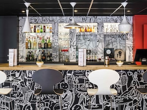 Eine Bar mit Wandgemälde in Schwarzweiß, Flaschenregalen und moderner Pendelleuchten.
