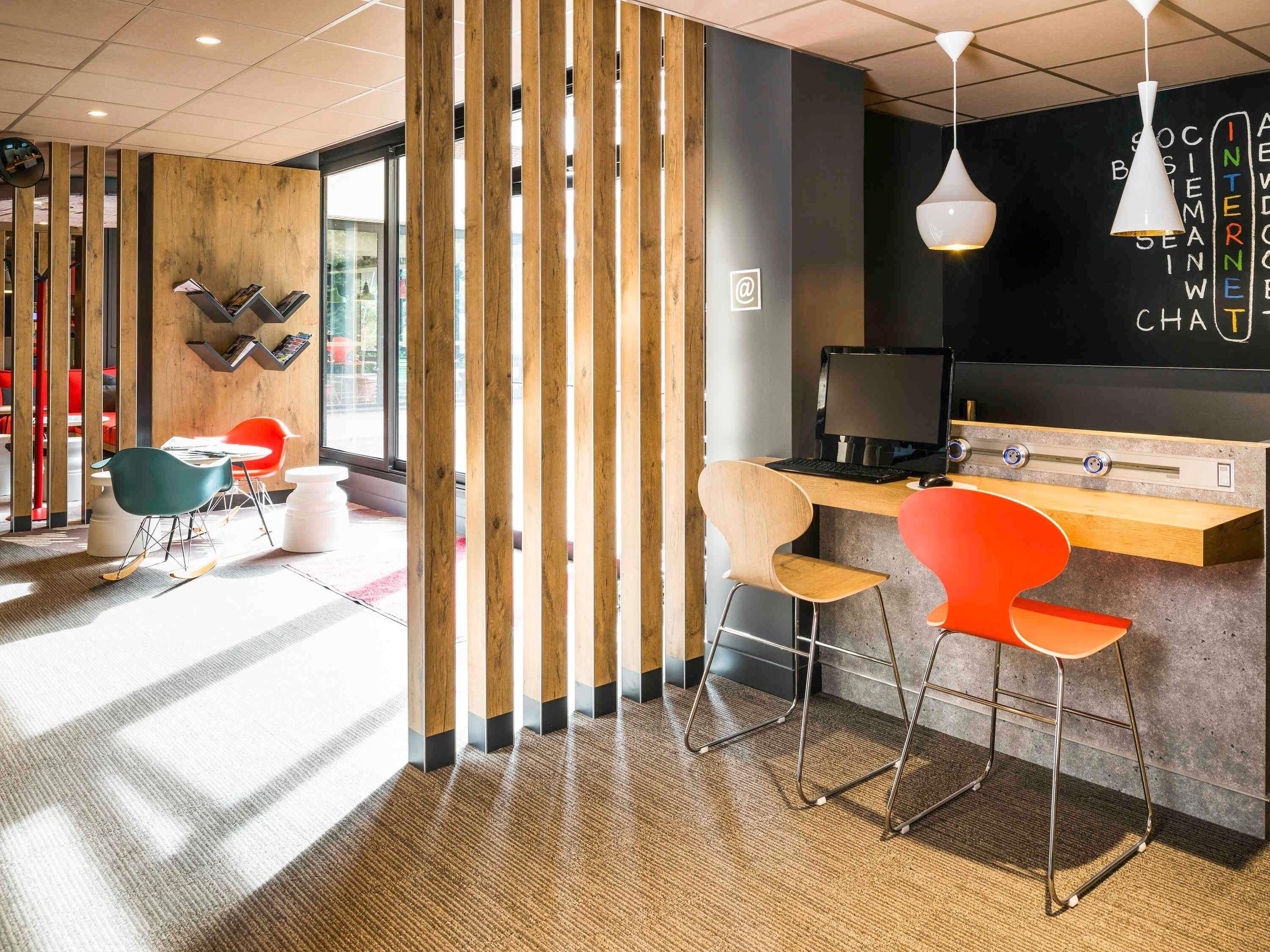 Un espace de travail moderne avec un séparateur en bois, un bureau avec un ordinateur et des chaises colorées.