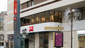 Um hotel moderno com uma placa grande da marca 'ibis', entrada de vidro e um poste de iluminação com luzes decorativas.