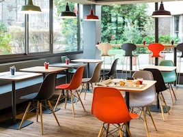 Interior moderno de una cafetería con mesas y sillas, ventanas amplias con vistas a zonas verdes e iluminación colgante.