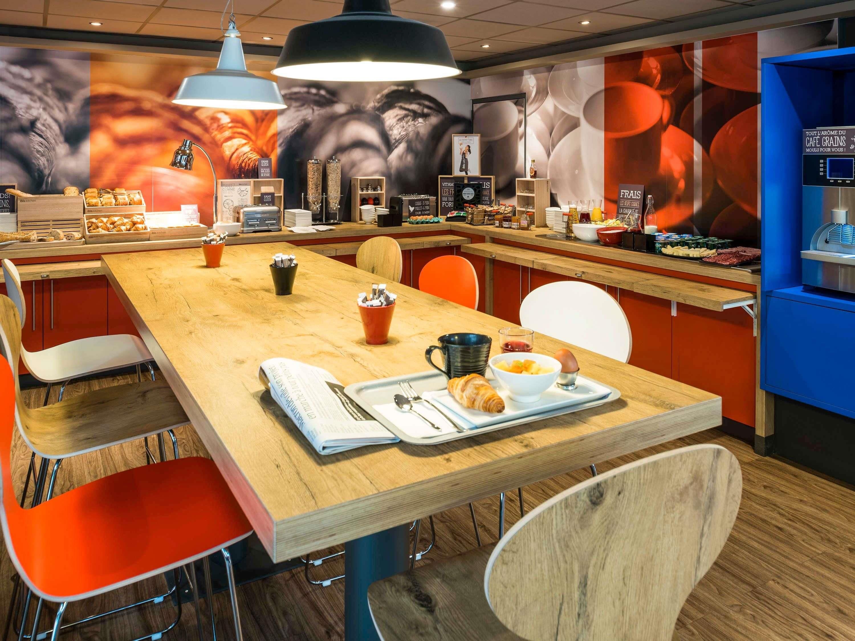 Un área de desayuno con una mesa de madera, sillas y una barra con alimentos.