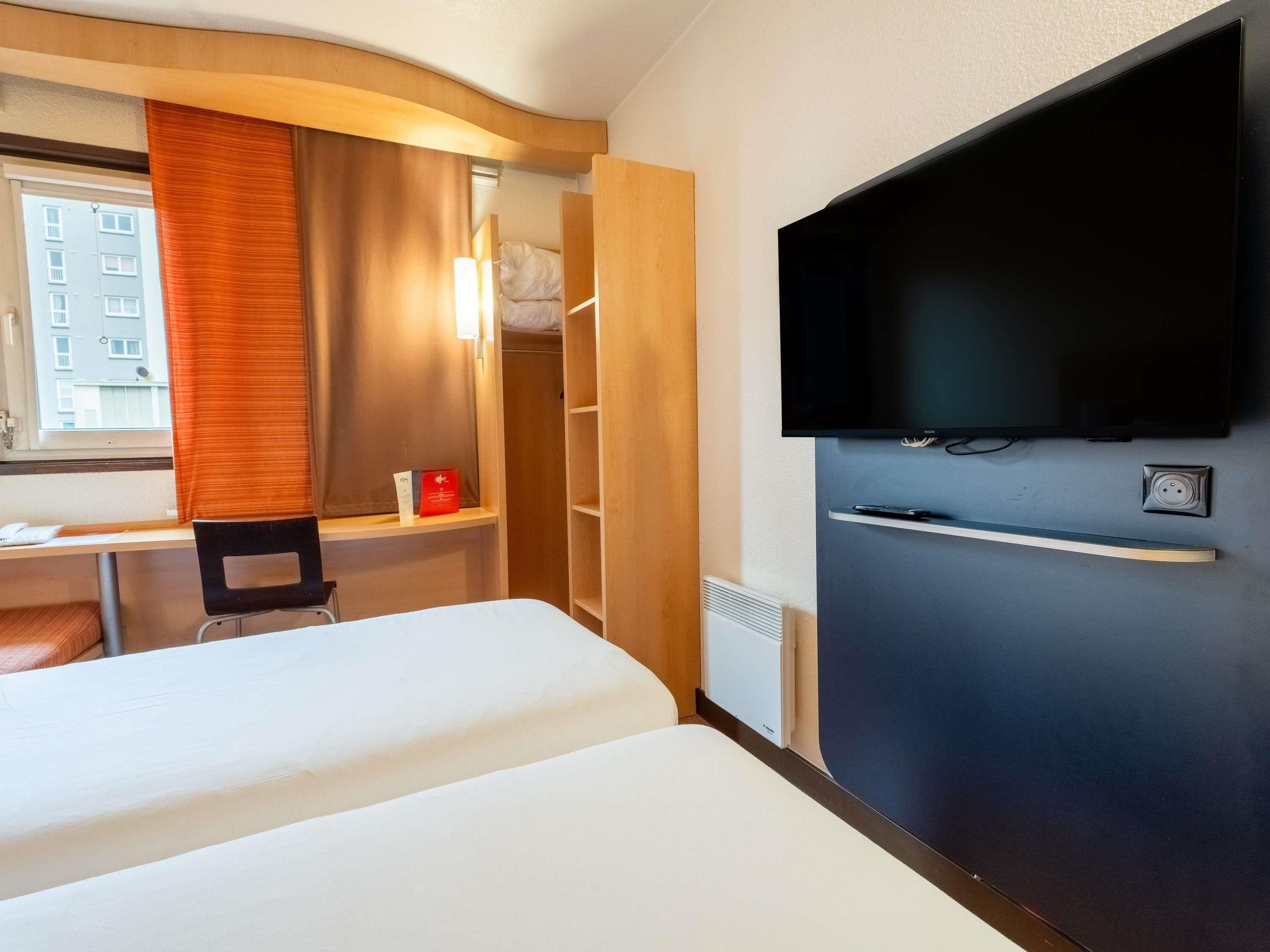 Une chambre d’hôtel comprenant un lit, un bureau, une chaise, une télévision et une armoire.