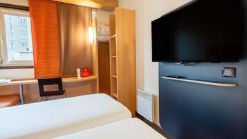 Une chambre d’hôtel comprenant un lit, un bureau, une chaise, une télévision et une armoire.
