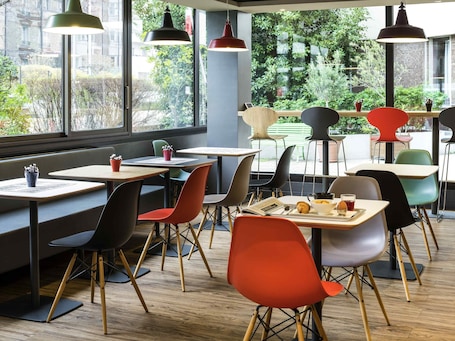 A modern cafe with tables, chairs, and hanging pendant lights.. ibis Paris Pont De Suresnes