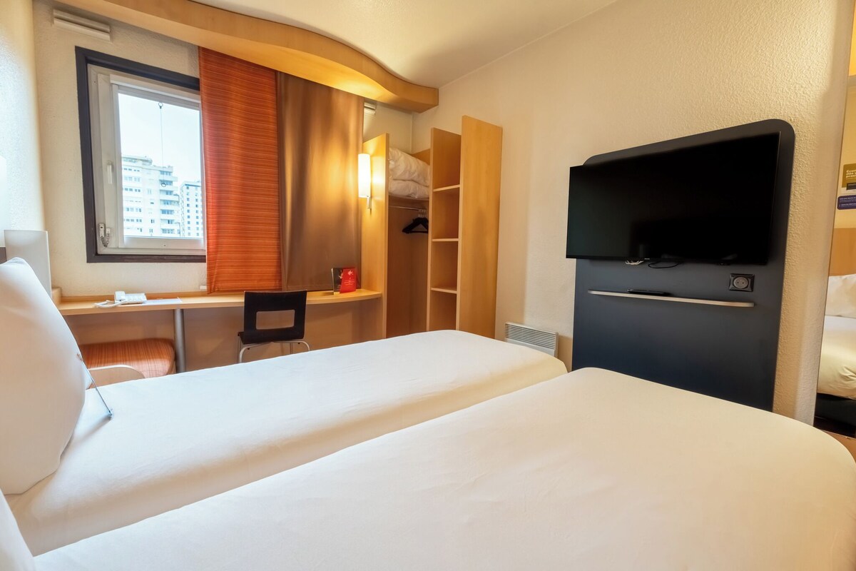 A hotel room with two beds, a desk, a chair, a TV, and a wardrobe.