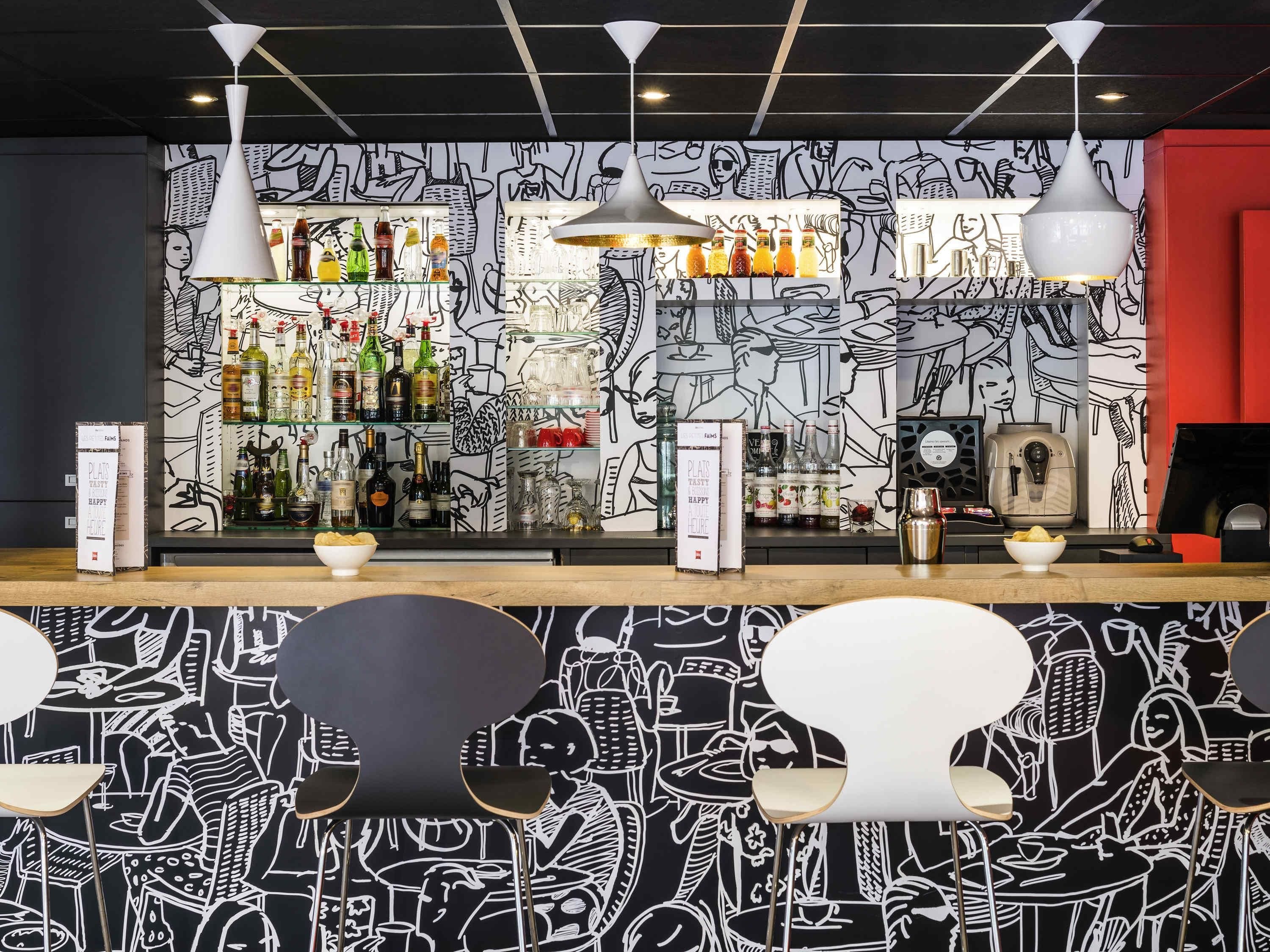 Un bar con un mural blanco y negro, estantes llenos de botellas de licor e iluminación colgante moderna.
