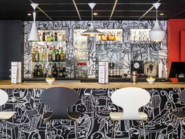 Un bar con un mural blanco y negro, estantes llenos de botellas de licor e iluminación colgante moderna.