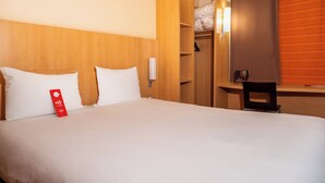 A hotel room with a bed, a wooden headboard, a wardrobe, and a bedside table with a lamp.
