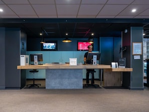 A reception desk with a computer, a sign reading 'KEY BOX,' and a monitor displaying a red screen. - ibis Paris Pont De Suresnes (Suresnes)