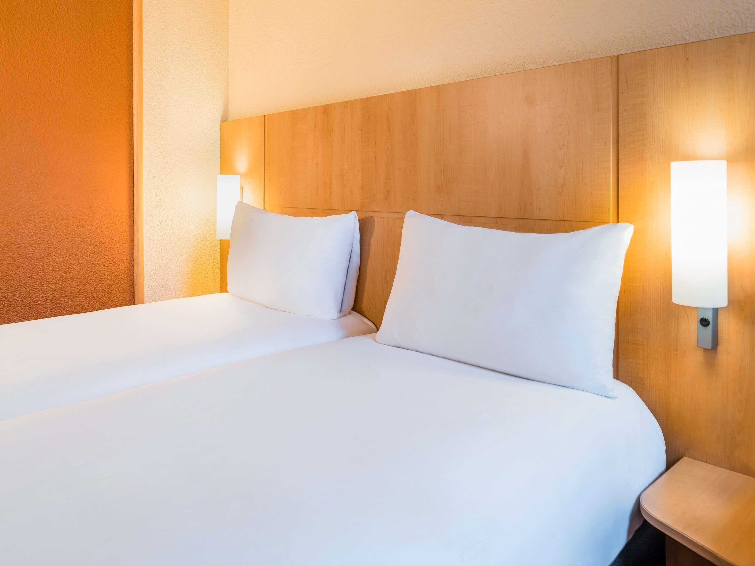 A hotel room with a wooden headboard, two bedside lamps, and a neatly made bed.