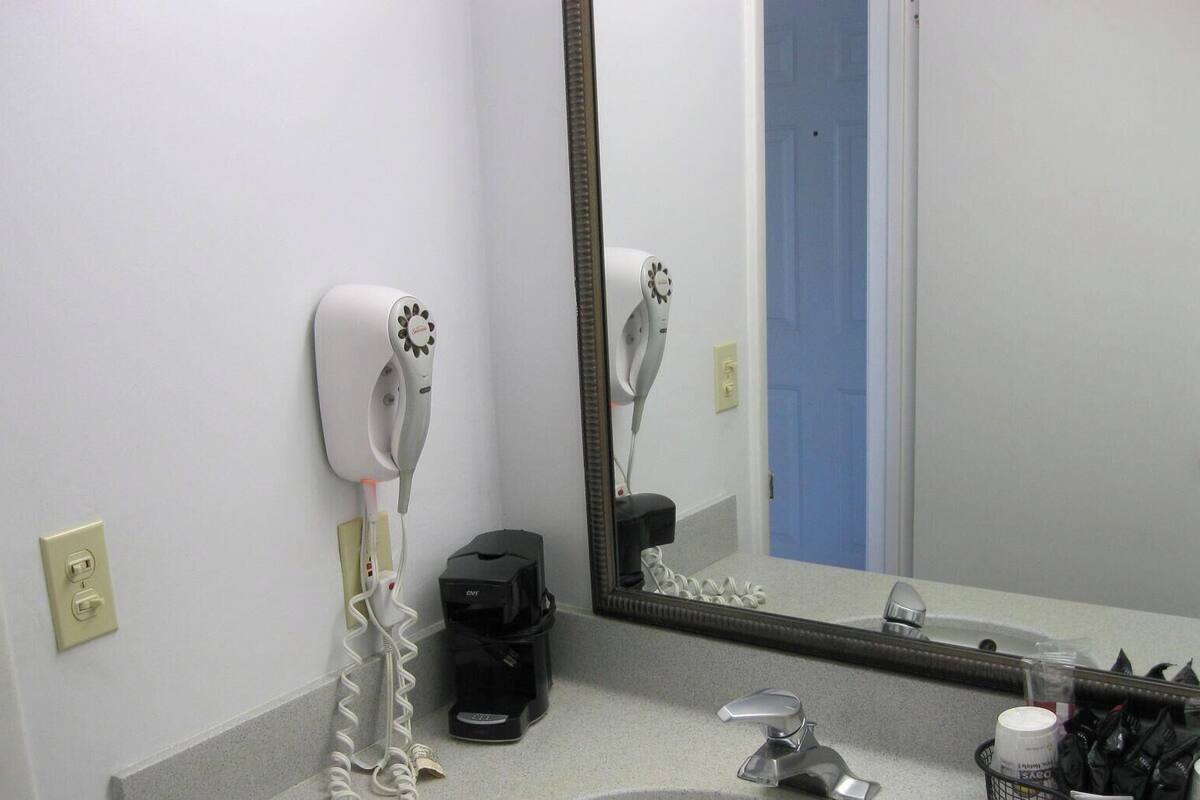 A hotel bathroom with a hairdryer, a coffee maker, and a mirror.