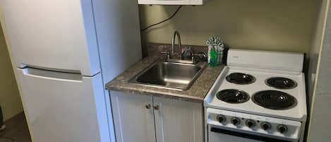 A compact kitchen with a refrigerator, microwave, sink, and stove.
