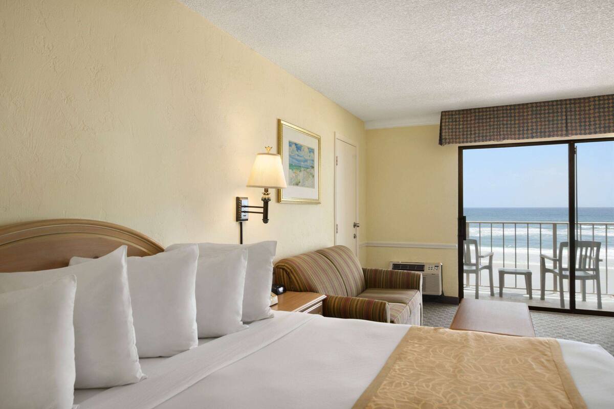 A hotel room with a large bed, a sofa, a desk, and a balcony with a view of the ocean.