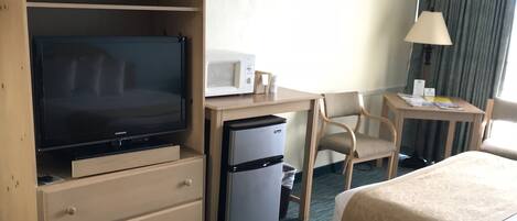 Quarto de hotel com televisão, micro-ondas, escrivaninha, cadeira e duas camas.