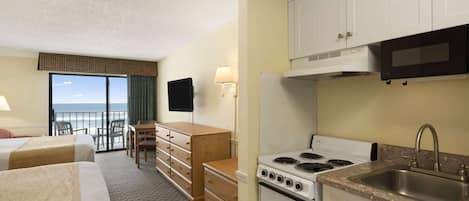 A hotel room with two beds, a kitchenette, a TV, a balcony with a view, and a desk with chairs.