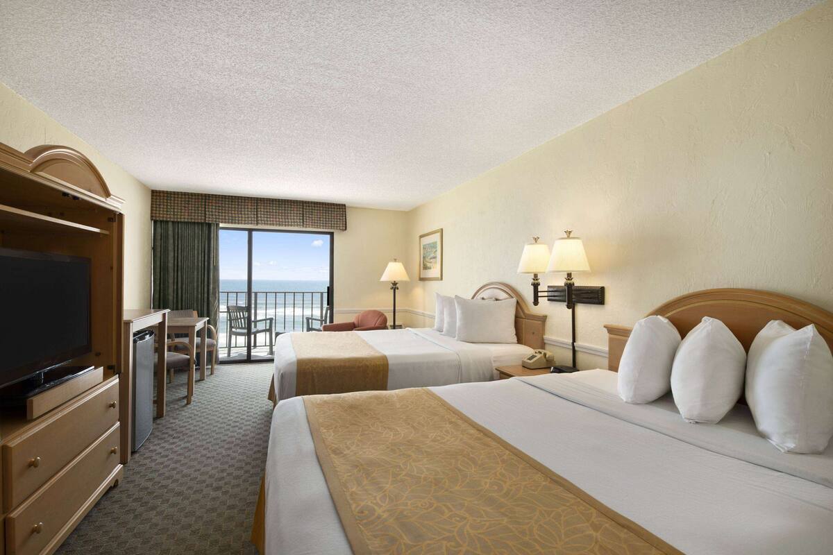A hotel room with two beds, a television, a desk, and a view of the ocean.