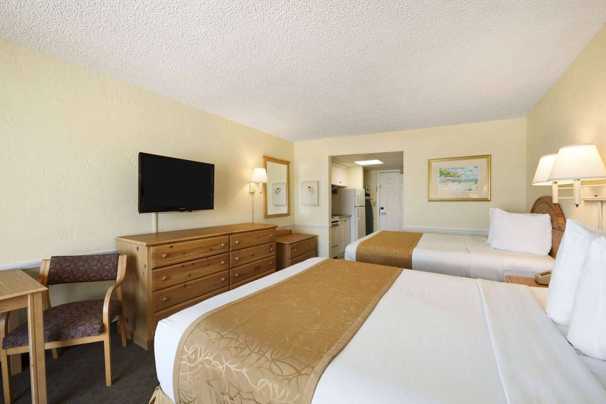 A hotel room with two beds, a desk, a chair, a dresser, a television, and a painting on the wall.