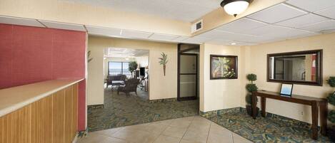 A hotel lobby with a reception desk, a seating area, a wall-mounted TV, and a patterned carpet.