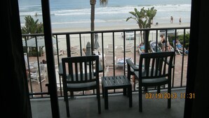 Een balkon met uitzicht op het strand, met stoelen en parasols.
