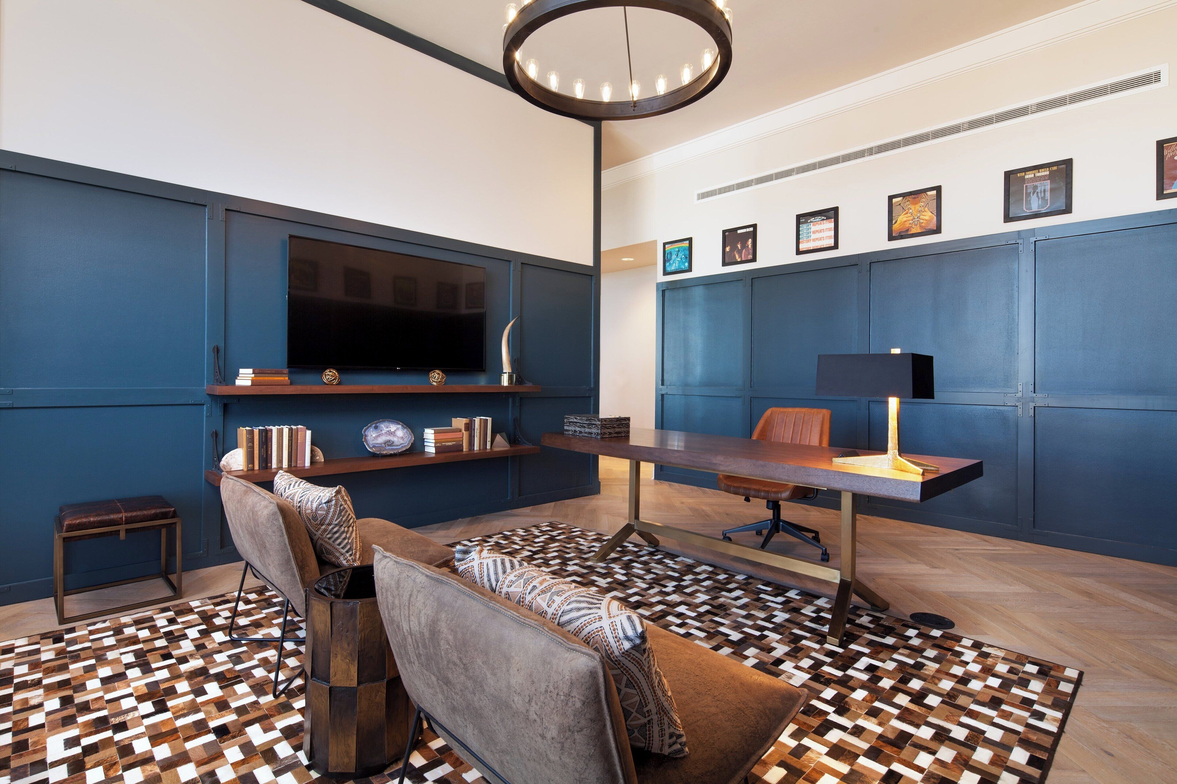 A modern living room with a large flat-screen TV, a wooden coffee table, a patterned rug, and a desk with a lamp.