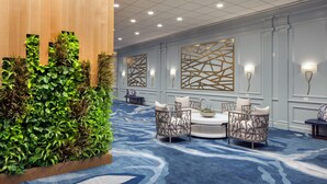 Un hall d’hôtel avec un tapis bleu, un mur lambrissé en bois et un espace détente comprenant une table et des chaises.