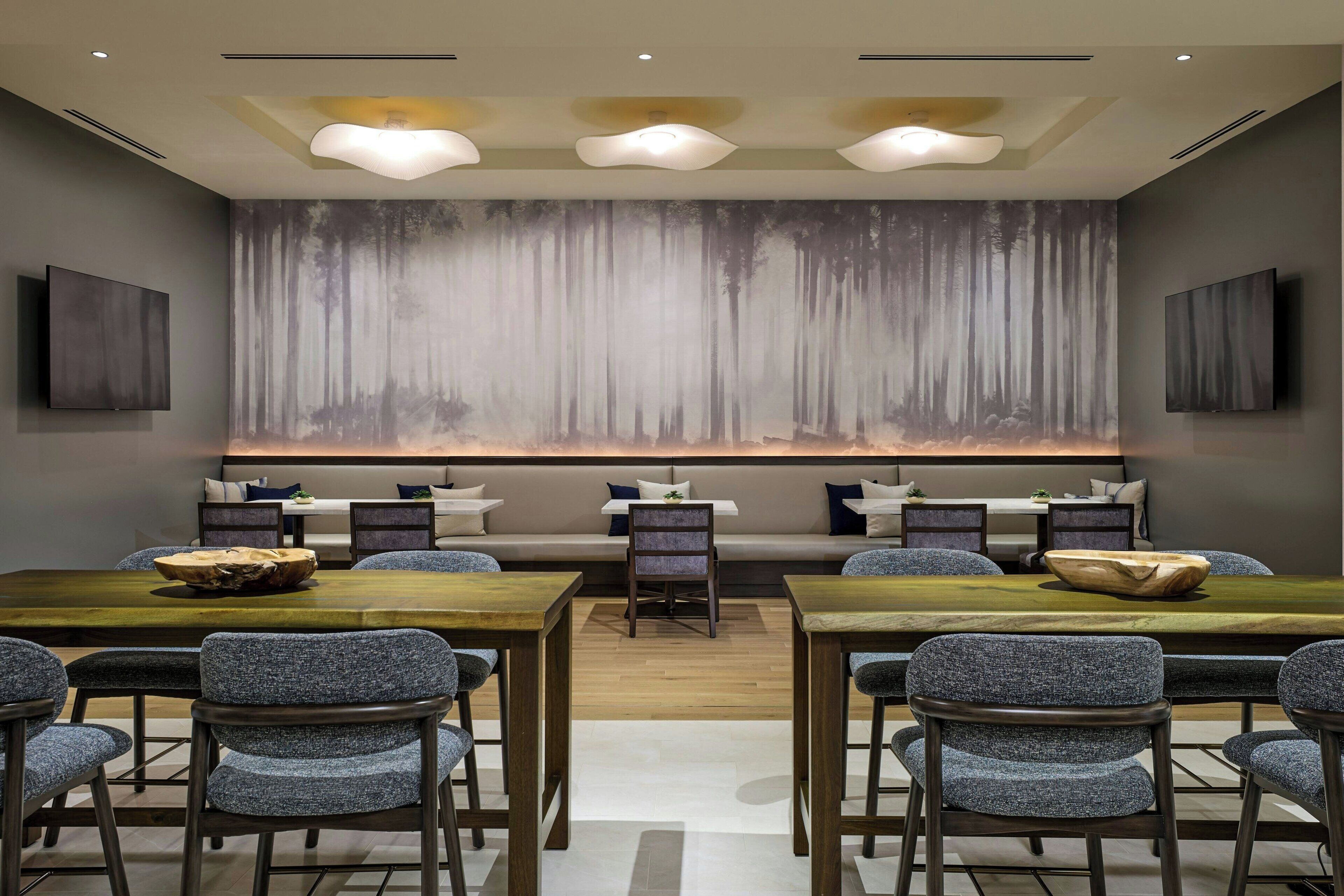A modern dining area with a long table, multiple chairs, and a large wall mural.