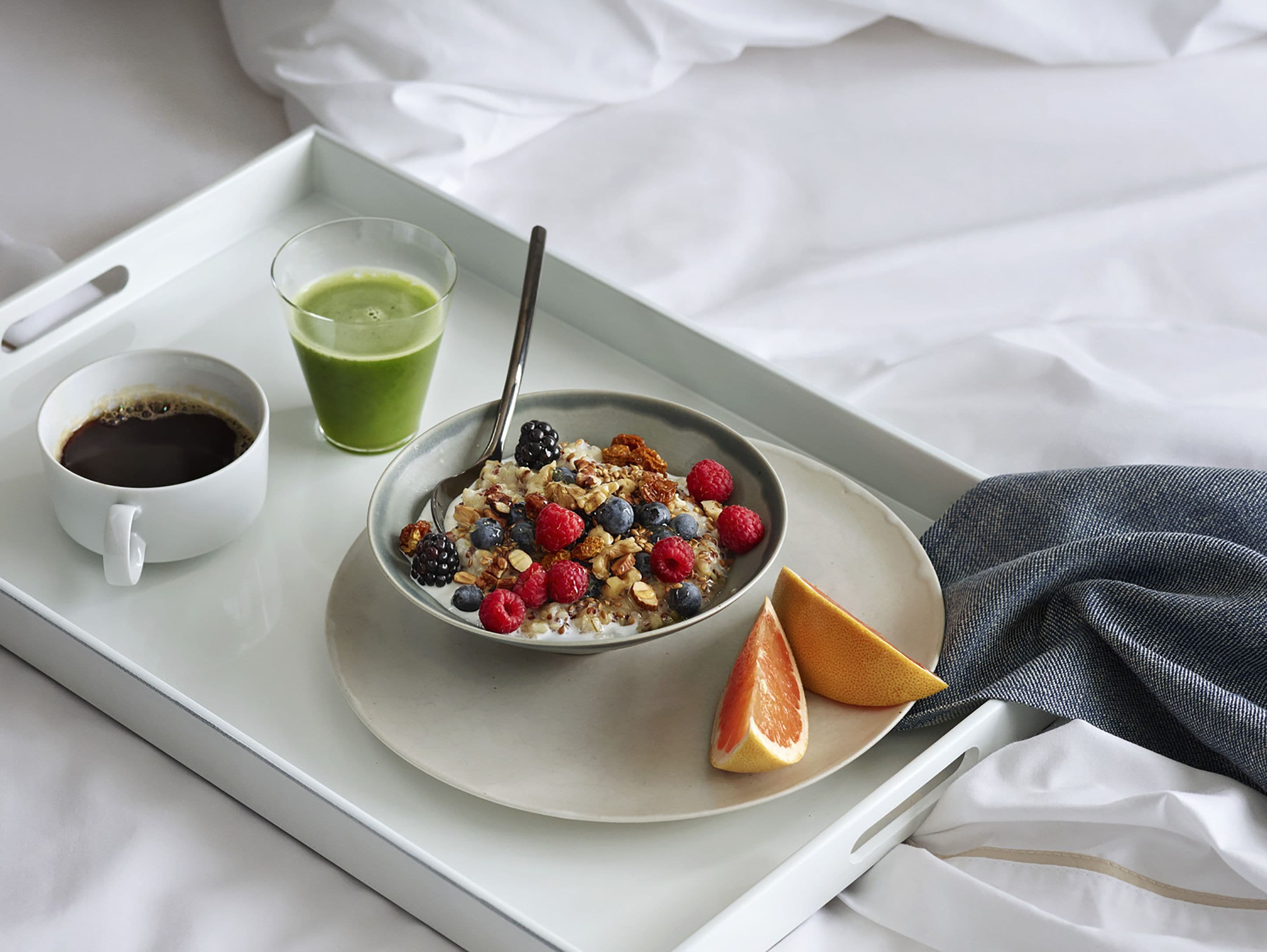 A breakfast tray with a bowl of cereal topped with berries and nuts, a cup of coffee, and a glass of green juice.
