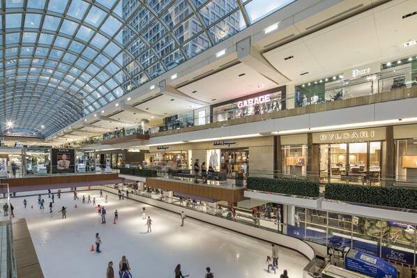 A multi-level shopping mall with a glass ceiling, featuring stores like 'Garage' and 'BVLGARI'.